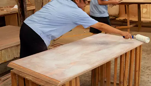 Workers apply the wood adhesive to the wooden boards with a brush.
