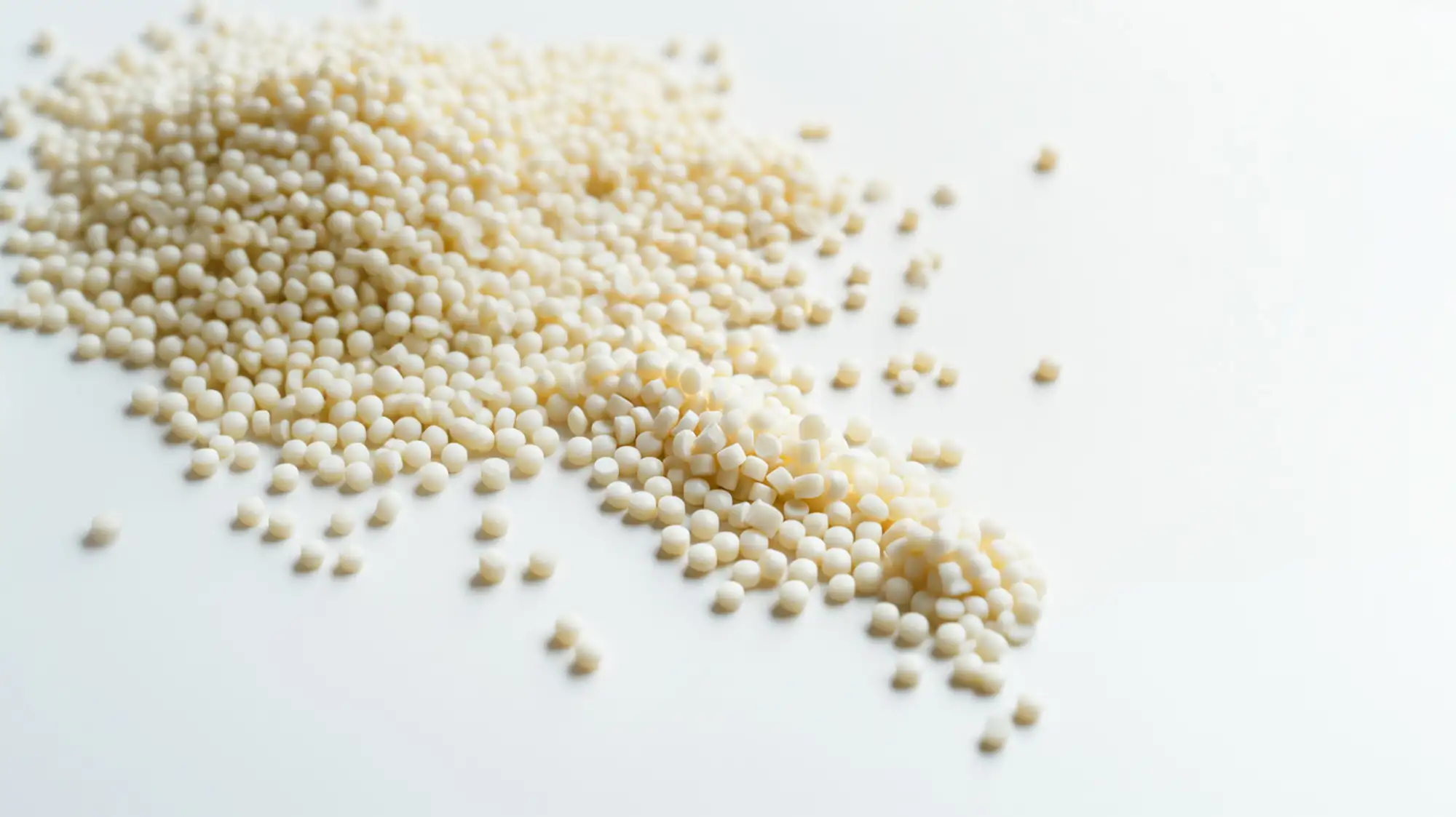 Milky white hot melt adhesive pellets scattered on a white studio background.