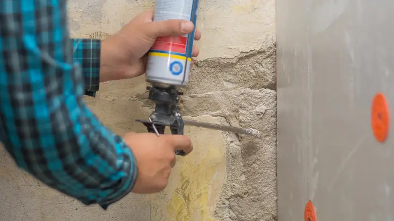 A worker holding a spray gun, preparing to apply adhesive to a wall; This is one of the common spray adhesive mistakes—inappropriate distance.